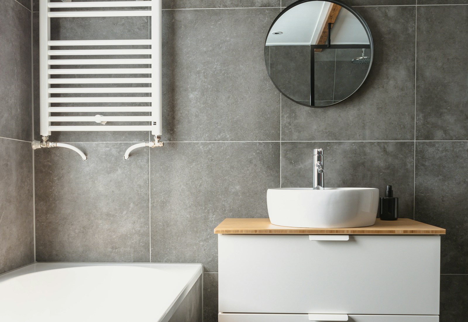 Refitted bathroom with grey stone tiles, white heated towel rail and white vanity unit with timber worktop